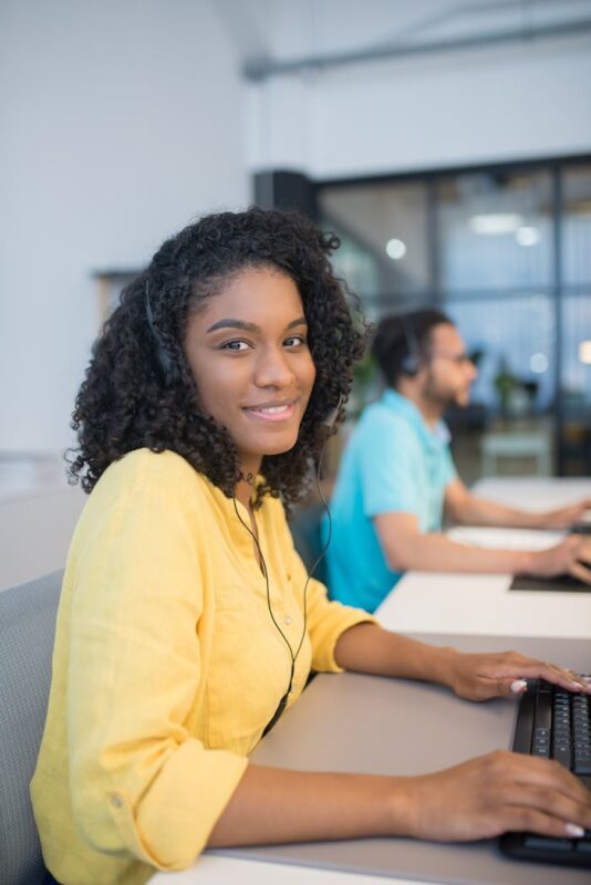 Young woman in a bright office, wearing headphones and working on a computer.